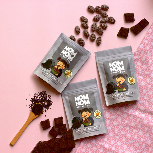 Three packages of 'NOM NOM' snacks on a pink background with scattered snacks.